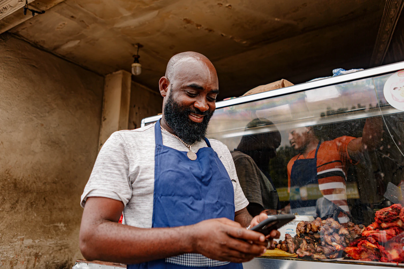 A shop owner in an apron checking his phone at his stall
